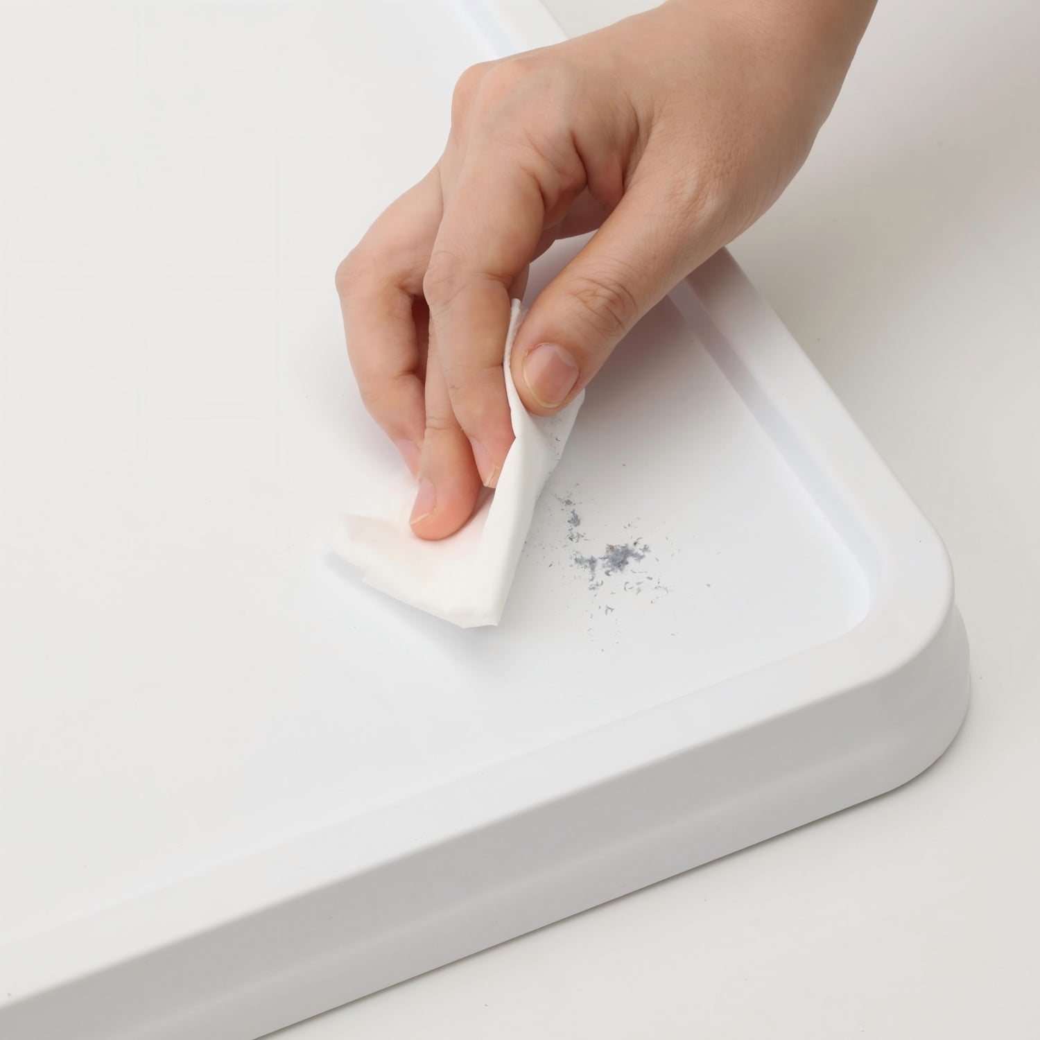 Hand wiping off dust or dirt from a white ABS puzzle board surface, demonstrating its easy-to-clean feature.