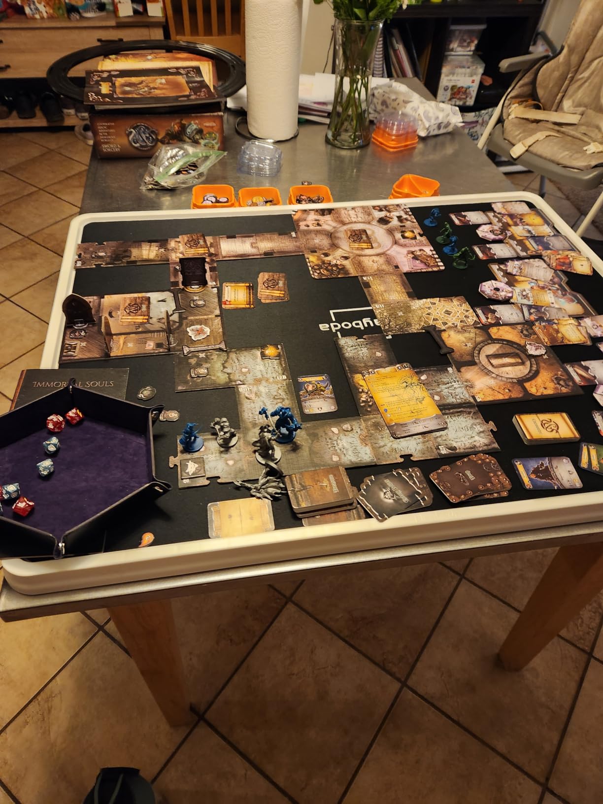 A Playboda puzzle board being used as a tabletop gaming setup, featuring a detailed dungeon board game layout with cards, dice, and miniature figures arranged neatly on the black surface.