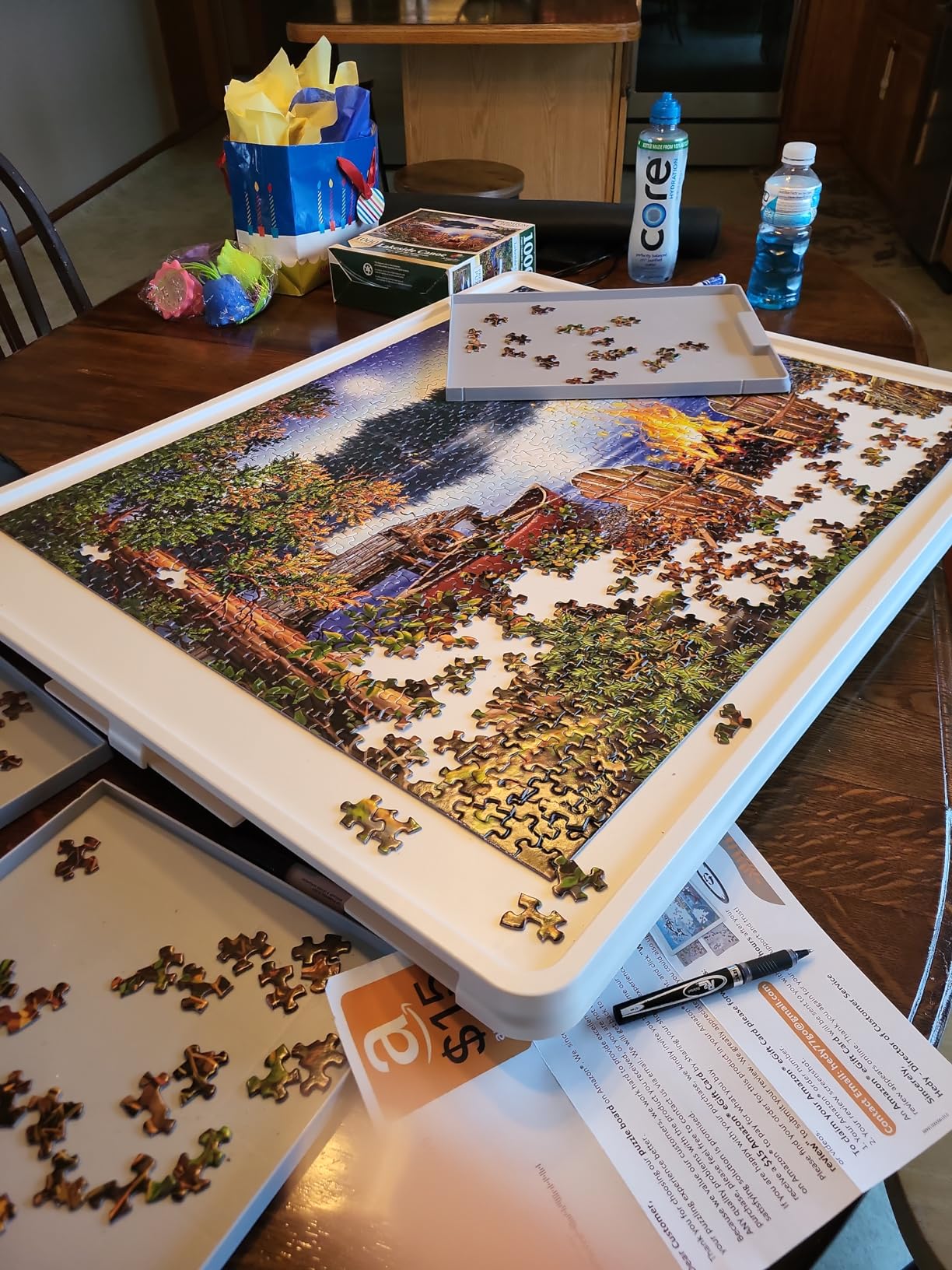 A white Playboda puzzle table tilted at an angle with a colorful jigsaw puzzle in progress, surrounded by sorting trays holding loose pieces.