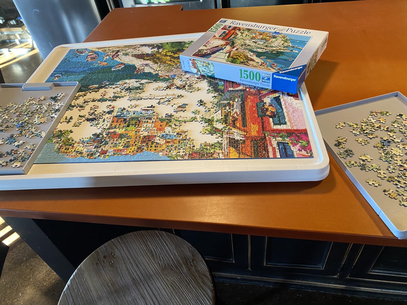 A 1500-piece jigsaw puzzle being assembled on a white Playboda puzzle board, with sorting trays and puzzle box placed on a wooden table.