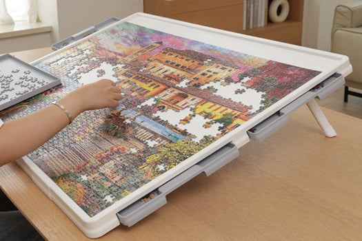 Person using a Playboda tilting puzzle board with drawers while assembling a jigsaw puzzle on a table